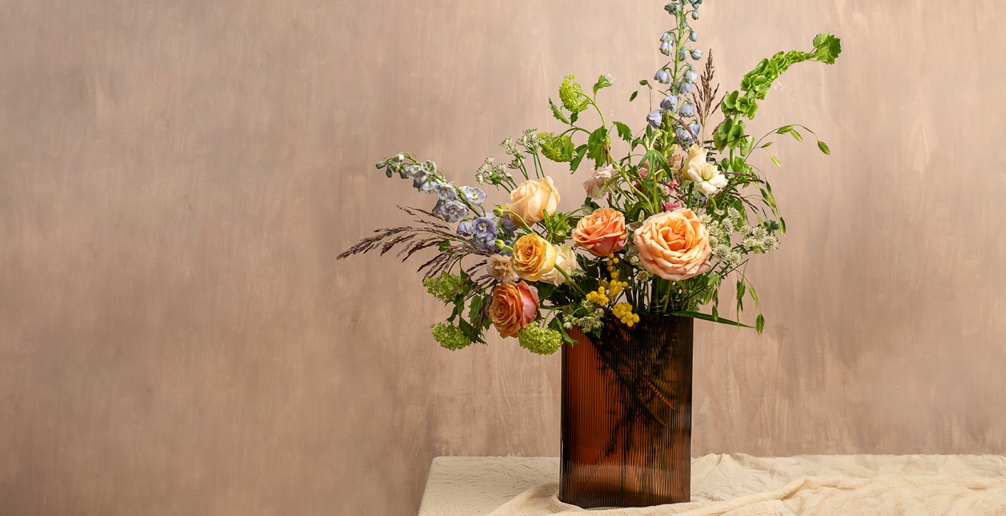 NUDE Mist vase in caramel lead free crystal, paired with tall blooms like delphinium, irises, foliage and grasses, created by Grace & Thorn