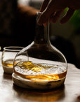 NUDE Glass Chill whiskey decanter with whiskey on a wooden table, hand reaching towards it.