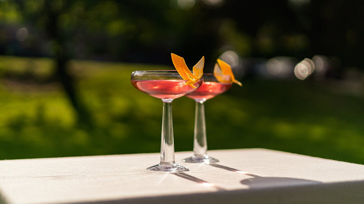 NUDE Big Top Coupe glass with a summer solstice cocktail in an outdoor setting
