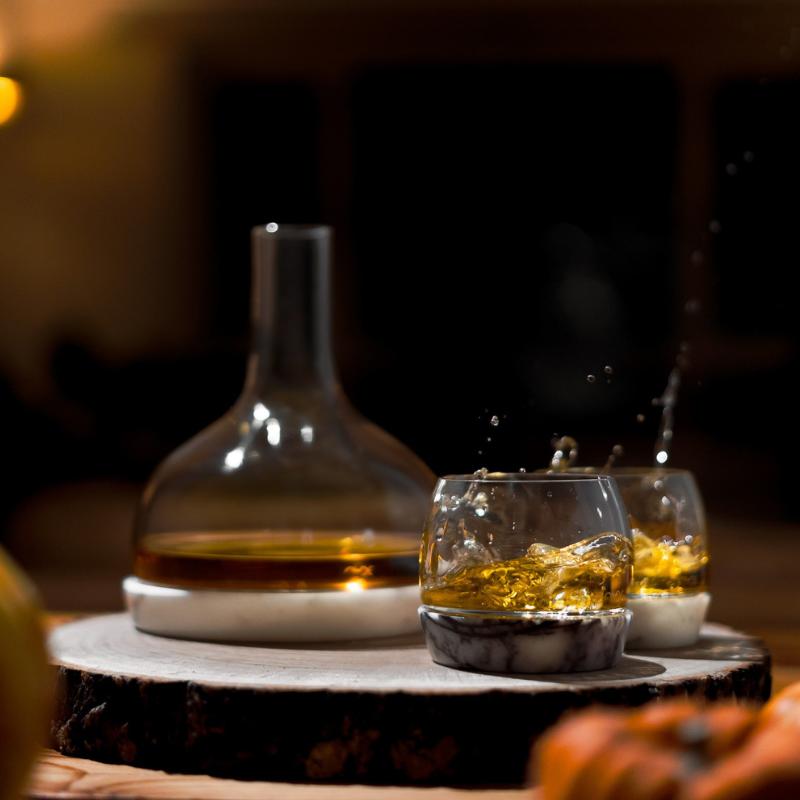 NUDE Chill whisky decanter and tumblers with marble base on wooden log slice with whisky splash by fireplace