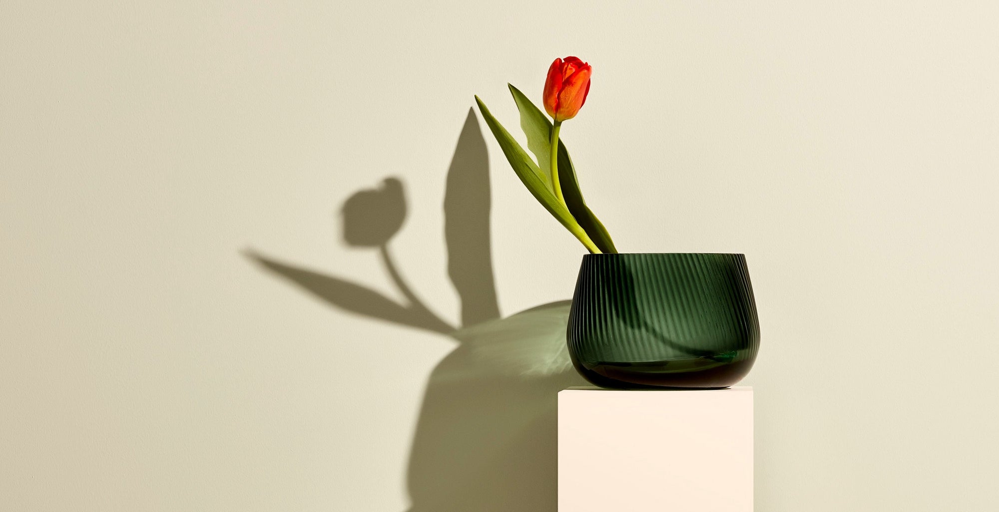 A home setting of a side supboard against a sage coloured wall, with various NUDE products; Mist vase wide in petroleum, the Big Top cocktail collection and the Joy votives in clear and steel blue