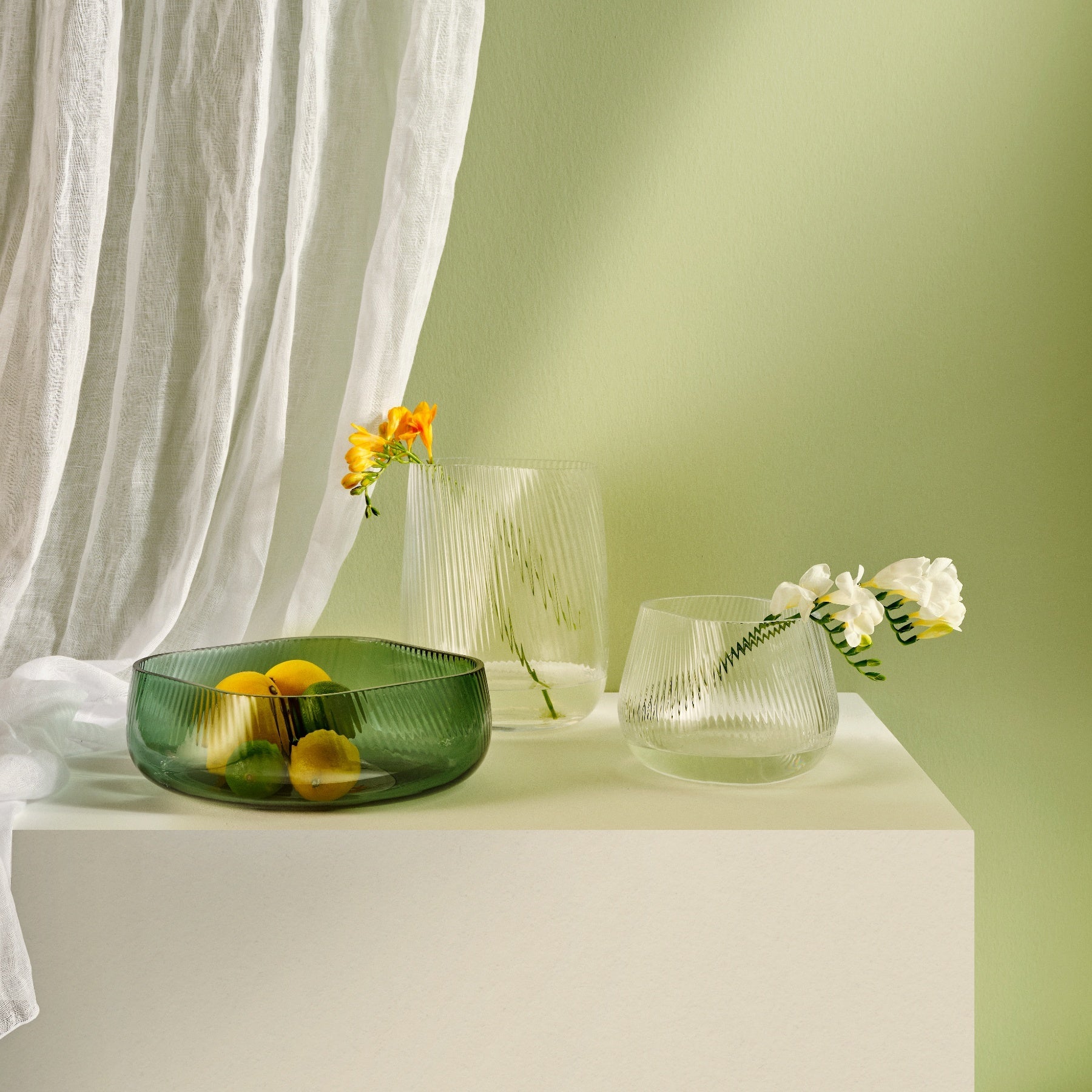 NUDE Opti vases with rippled design in clear and green, on a table with green background and some spring flowers in them