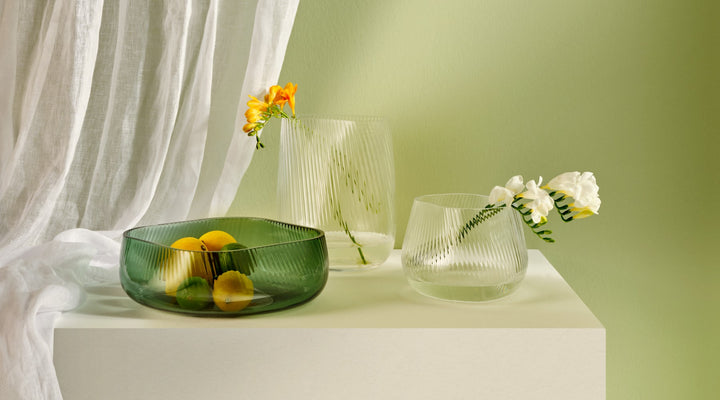 NUDE Opti collection of tall and medium vase in clear, and the centerpiece in green, with teh ribbed glass effect, presented with some single flowers