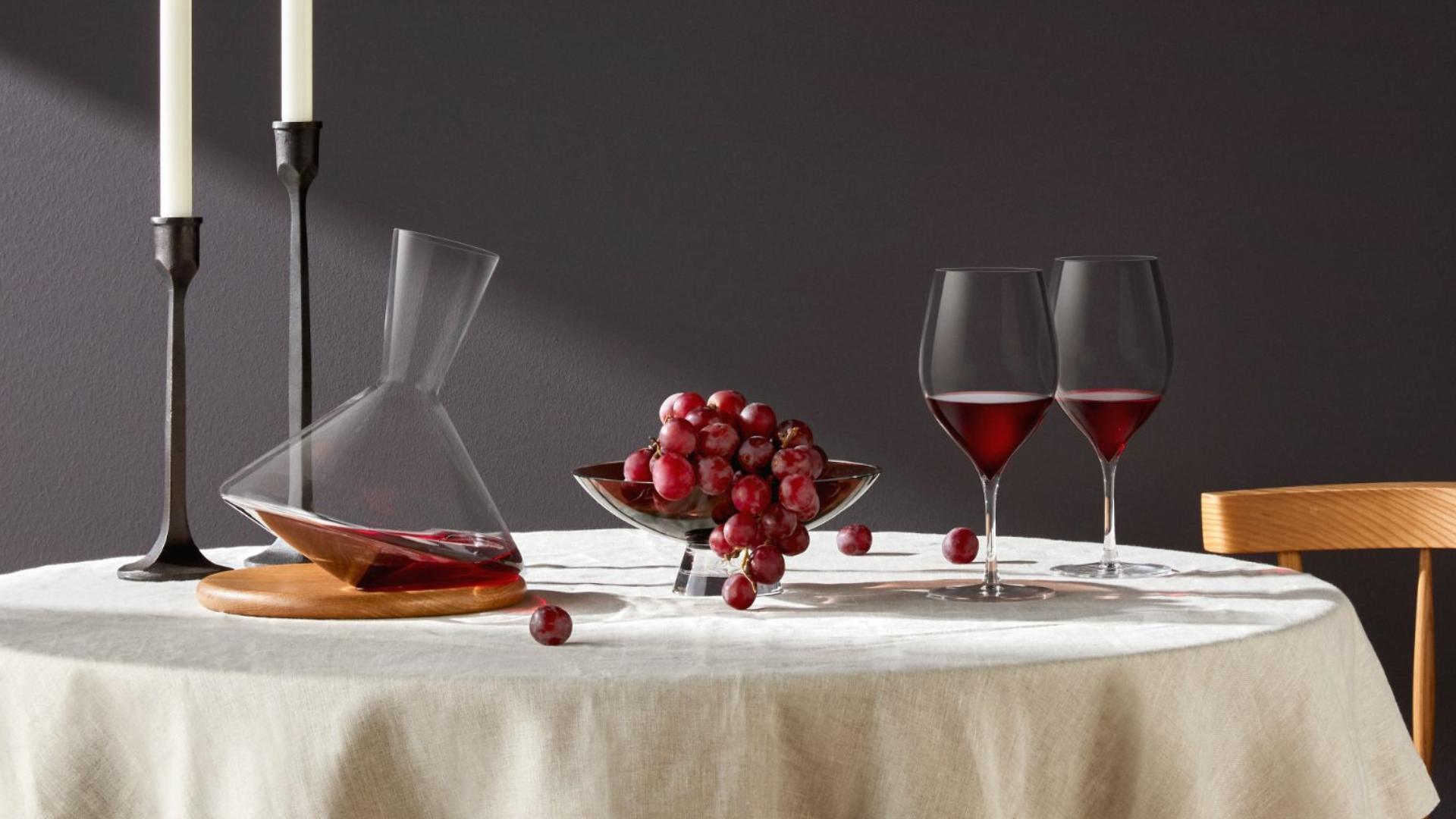 NUDE Terroir red wine glasses with Balance wine decanter on wooden board, styled with iron candle holders, grapes and Mono pendant lamp on a linen dining table