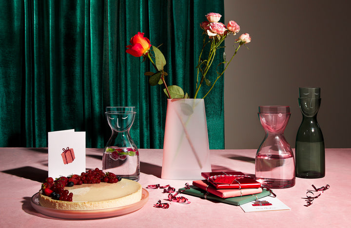 NUDE Mr&Mrs night water set in clearn, dusty rose and green presented on a pink table with the Pigmento pitcher in sandblasted ombre glass with red and pink roses