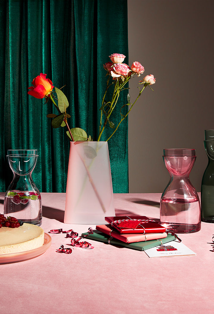 NUDE Mr&Mrs night water set in clearn, dusty rose and green presented on a pink table with the Pigmento pitcher in sandblasted ombre glass with red and pink roses