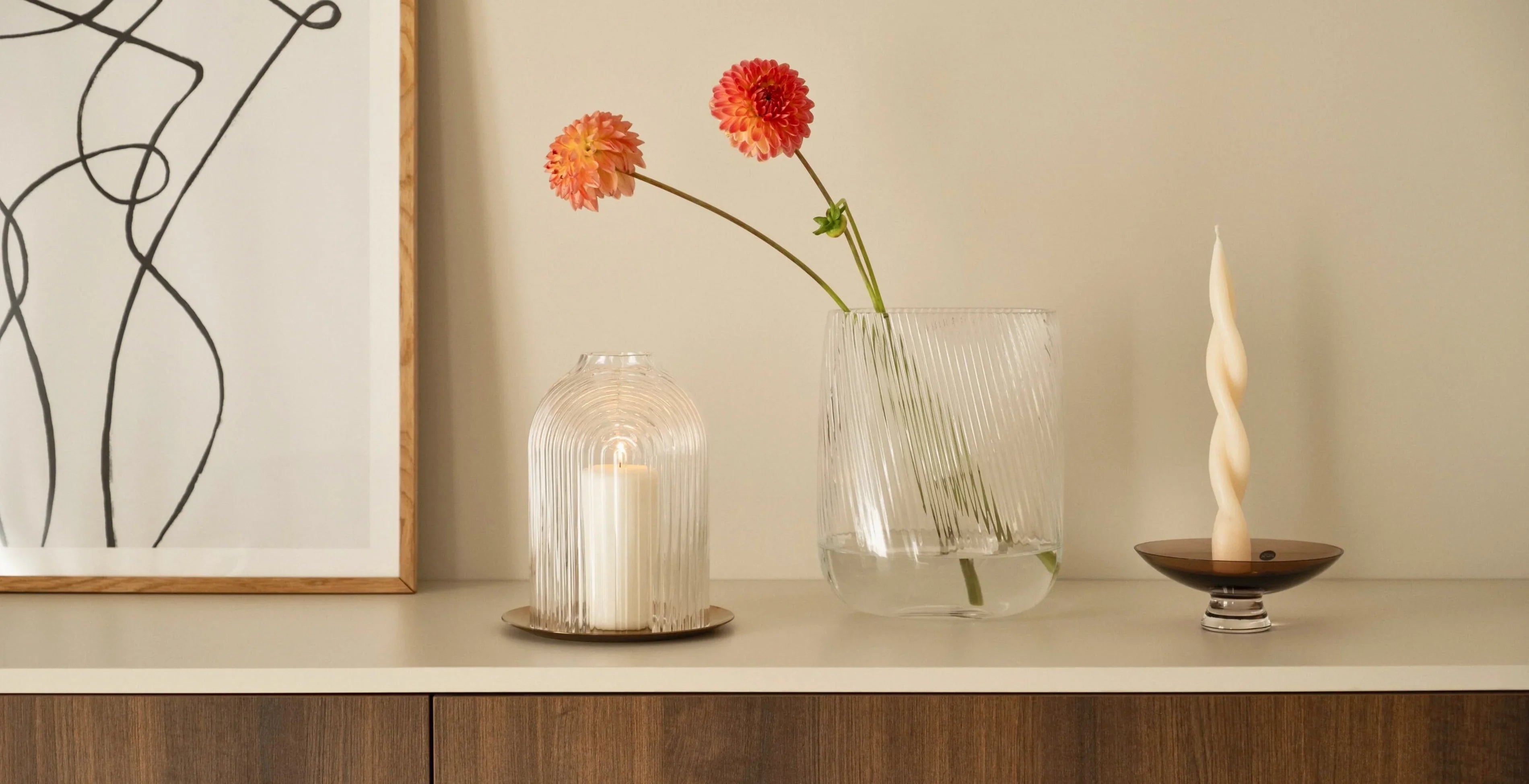 NUDE Decorative items including Ilo candle holder, Opti Vase with flowers and small bowl on a shelf against a beige wall.
