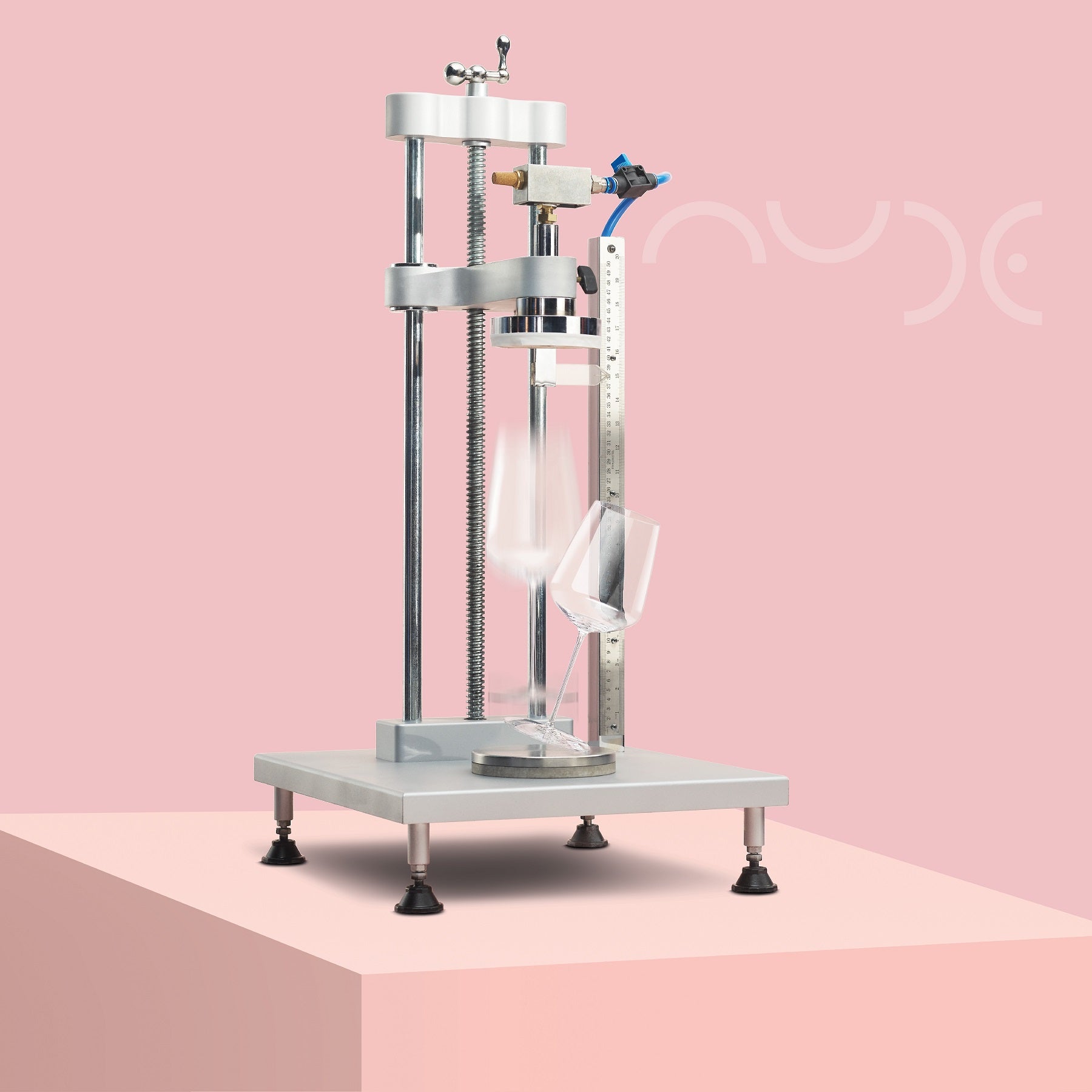 Mechanical device doing a free fall test of a glass on a pink background with the NUDE logo - inhouse test