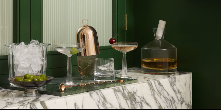 A cocktail bar setting with NUDE Alba carafe, Hepburn shaker with brass lid, Hemingway ice bucket and Big Top coupe glass and Alba DOF whisky glass.