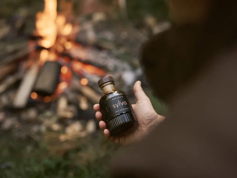 Hand holding a bottle labeled 'Sylva' in front of a campfire