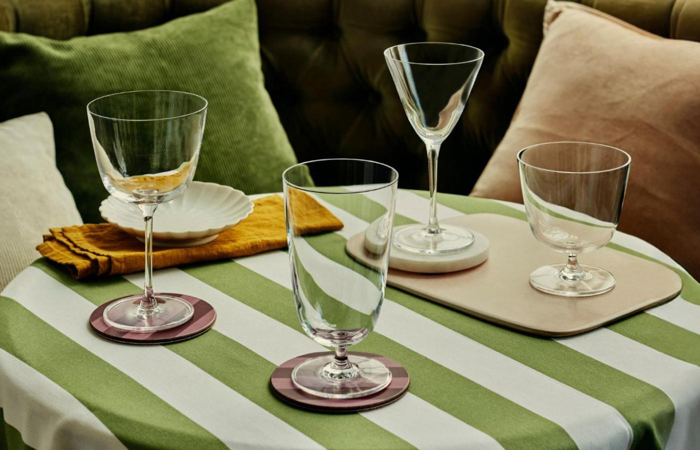 Four empty NUDE Bar/Giani glasses on coasters on a green-and-white striped vintage table.