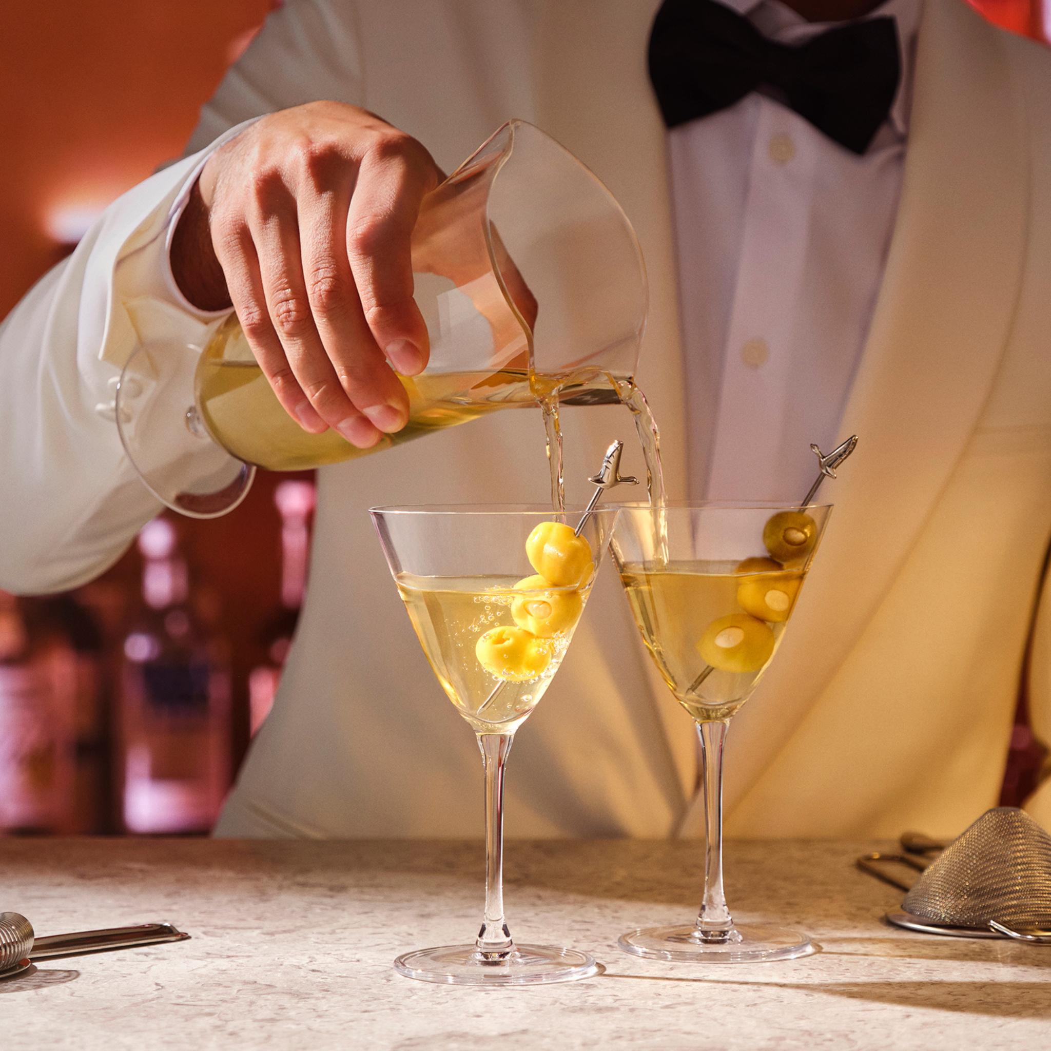 A bartender in a white dinner jacket pouring two martinis at once from the NUDE Bar/Giani Double Pour Mixing Glass