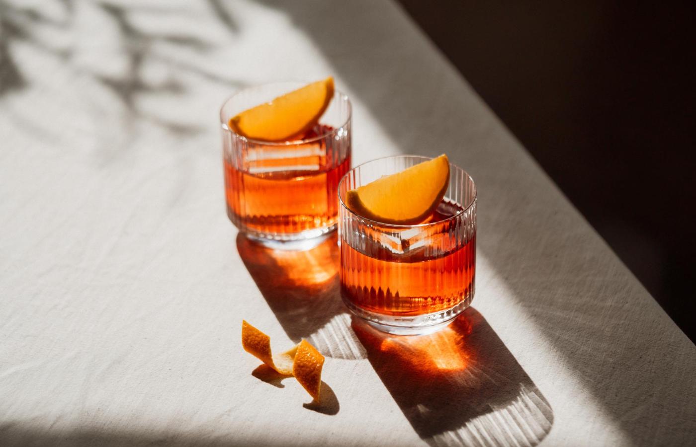 Two NUDE Big Top glasses holding Mediterranean Negronis, garnished with orange, in warm sunlight