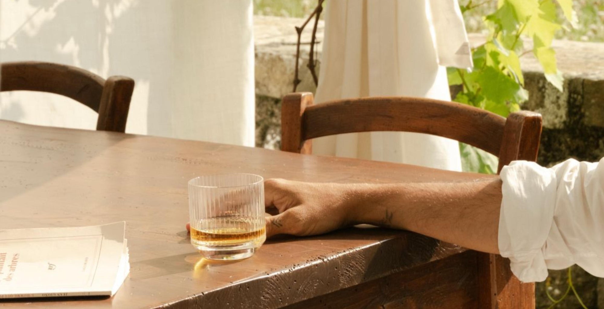 Person holding a NUDE Glass Big Top whiskey glass at a wooden table outdoors
