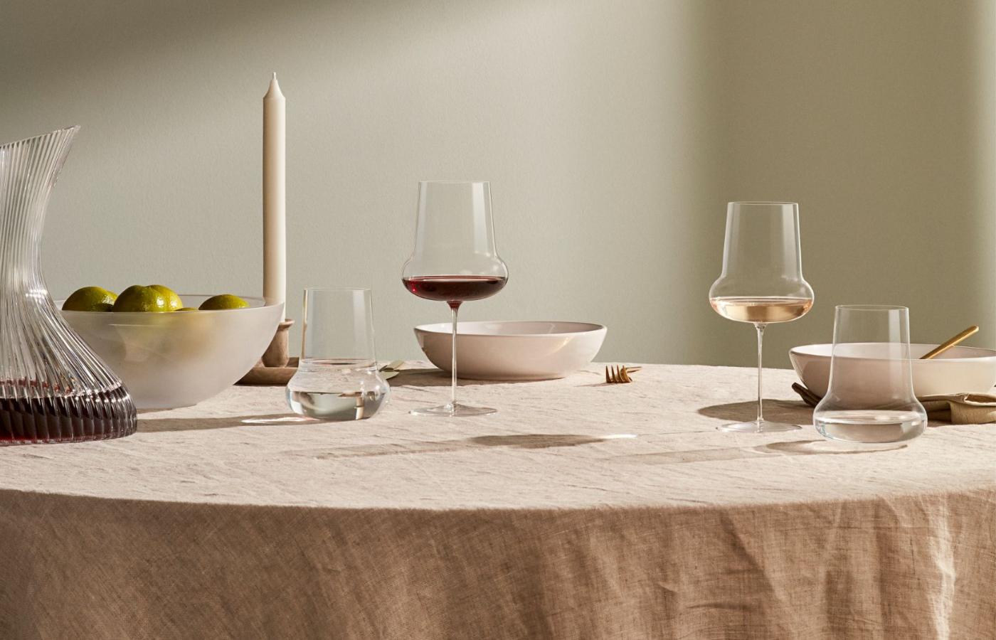 NUDE Ghost Zero Belly red wine glass and water glass with a fluted Vini carafe on a linen table in warm sunlight