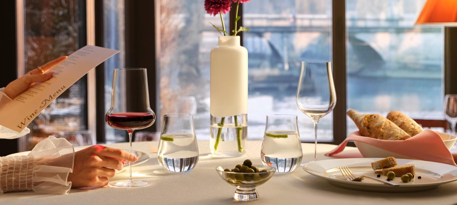 NUDE Ghost Zero Belly red wine glass, Tulip glass and water glasses with a Silhouette bowl on a restaurant table with a wine menu and a riverside view