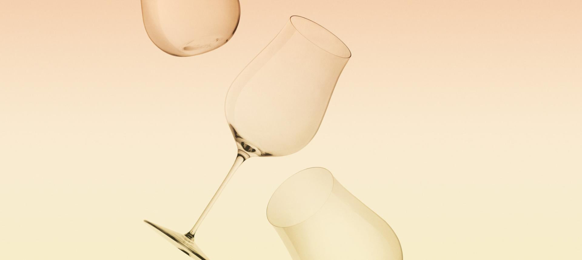 Three NUDE Ghost Zero wine glasses floating against a peach and yellow gradient background, illustrating their feather-light weight