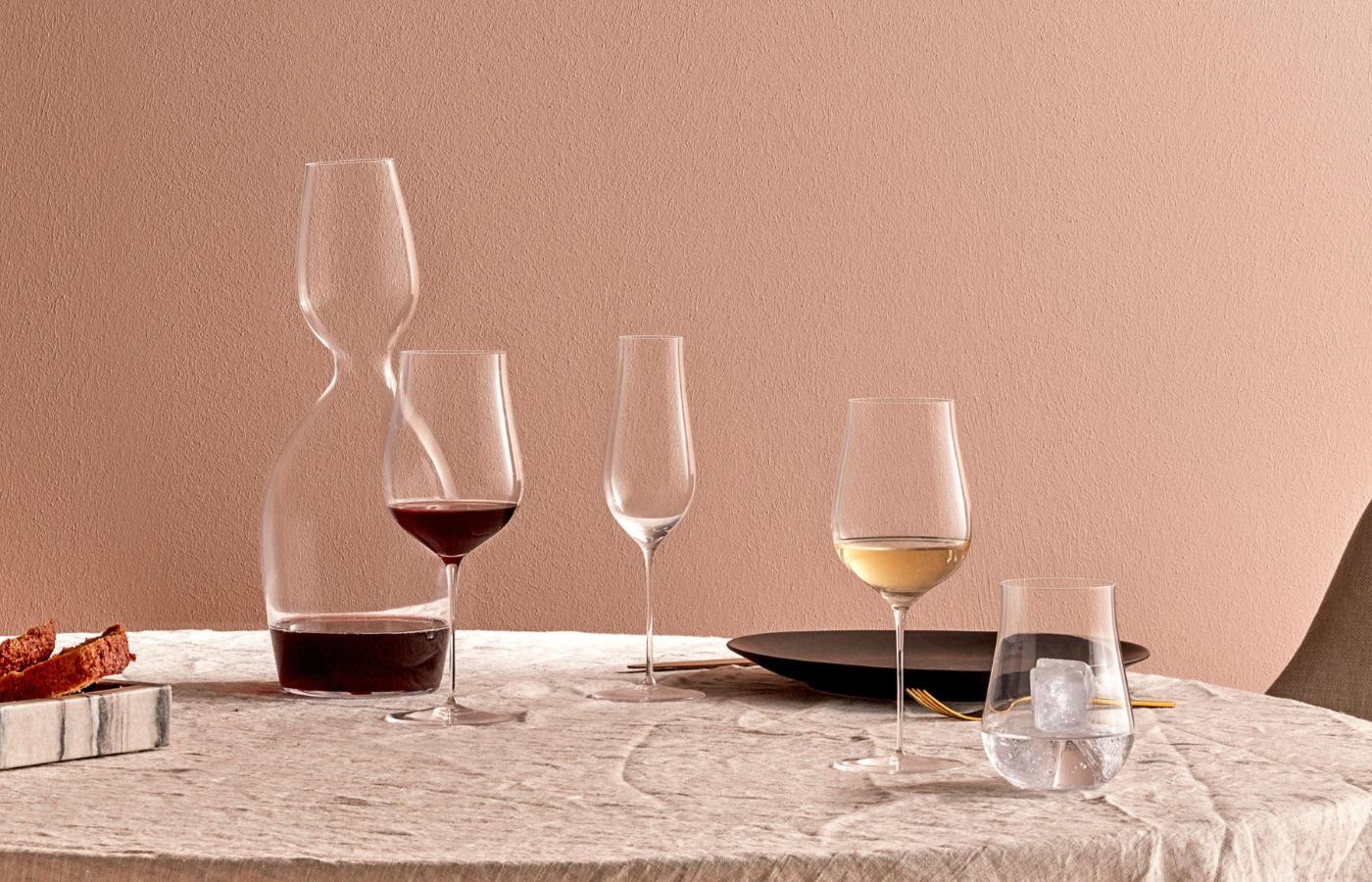 NUDE Ghost Zero Tulip red wine glass, white wine glass, champagne flute and water glass with a Red Or White water carafe on a linen table against a warm terracotta wall