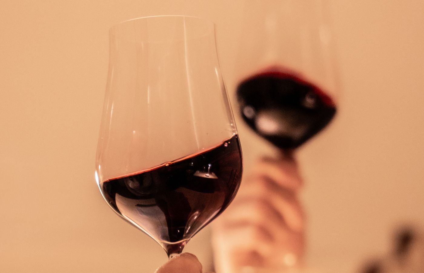 NUDE Ghost Zero Tulip Red Wine Glass held in close-up, glasses raised in a toast with a soft-focus background.