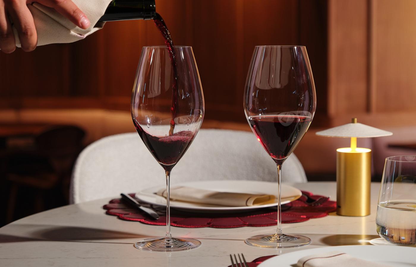 NUDE Stem Zero Grace glasses, red wine being served at a restaurant table setting with warm wood paneling and gold table lamp
