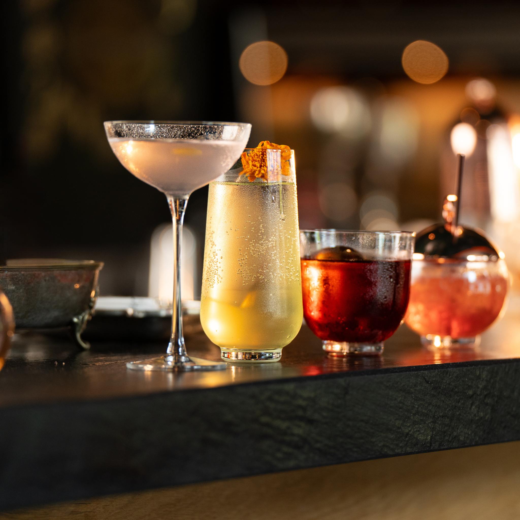 NUDE Hepburn coupe, longdrink, lowball and alchemy glasses with cocktails in a dark, warmly lit bar