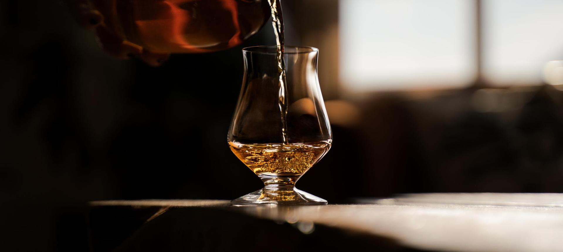 Whisky being poured into a NUDE Islands tasting glass in warm backlight
