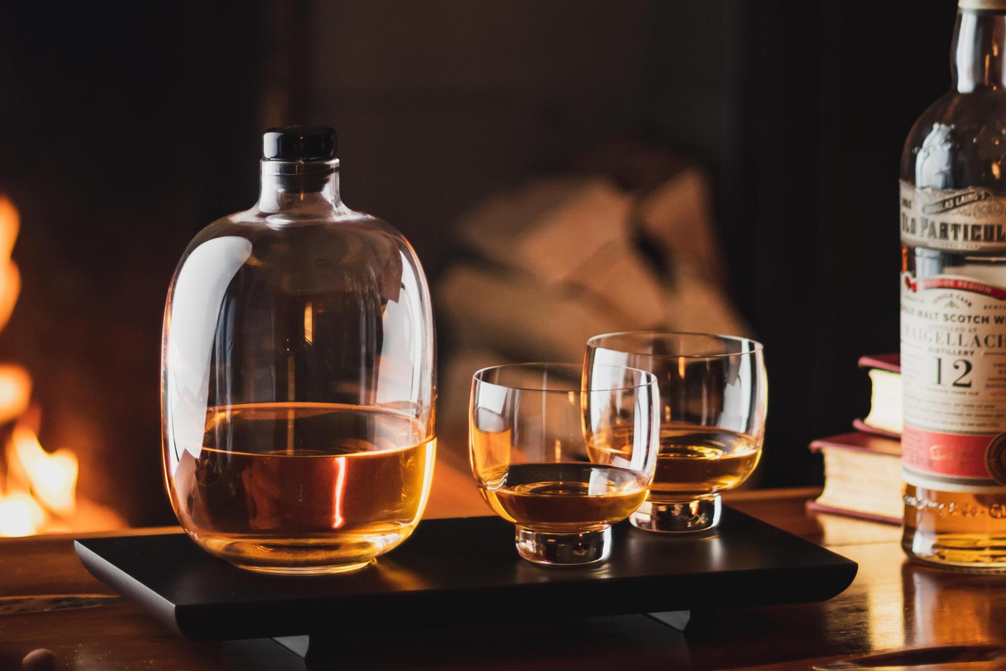 NUDE Malt whisky decanter and glasses by a fireplace