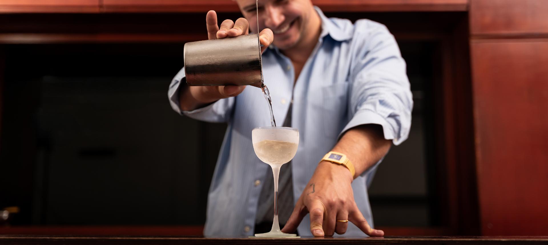 Rémy Savage pouring a cocktail into a frosted NUDE Savage Pony Glass behind a bar.
