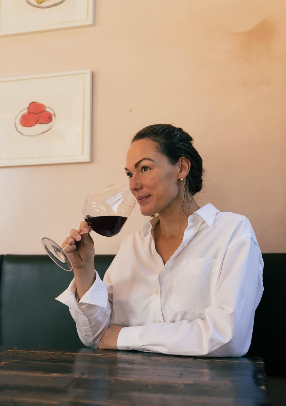 Honey Spencer sipping red wine from a NUDE Stem Zero Elegant Red Wine Glass beside artwork at Sune