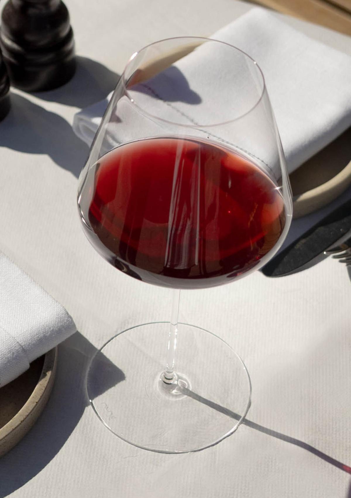A NUDE Stem Zero Elegant Red Wine Glass Medium filled with red wine on a sunlit linen table setting