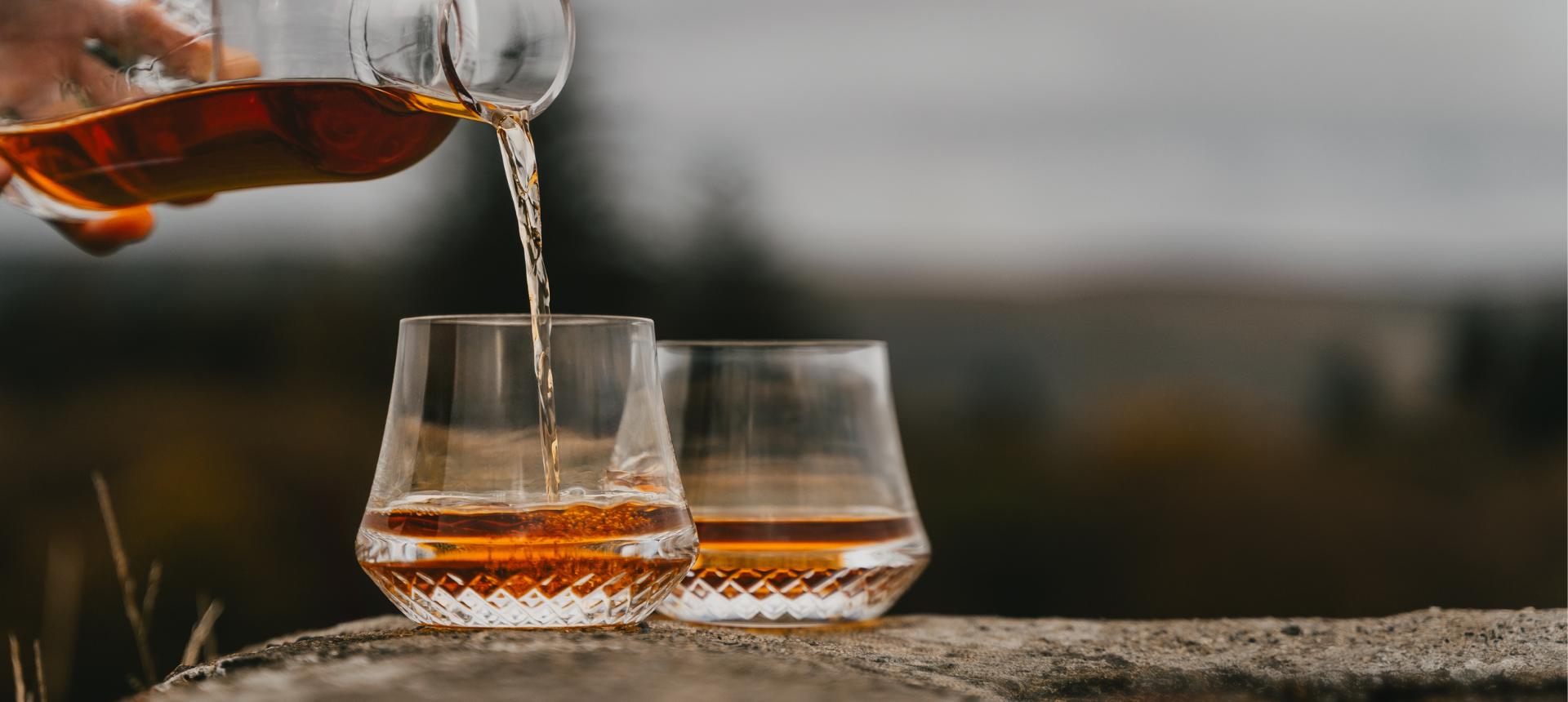 Whisky being poured into two NUDE whisky glasses on a stone ledge in the Highlands