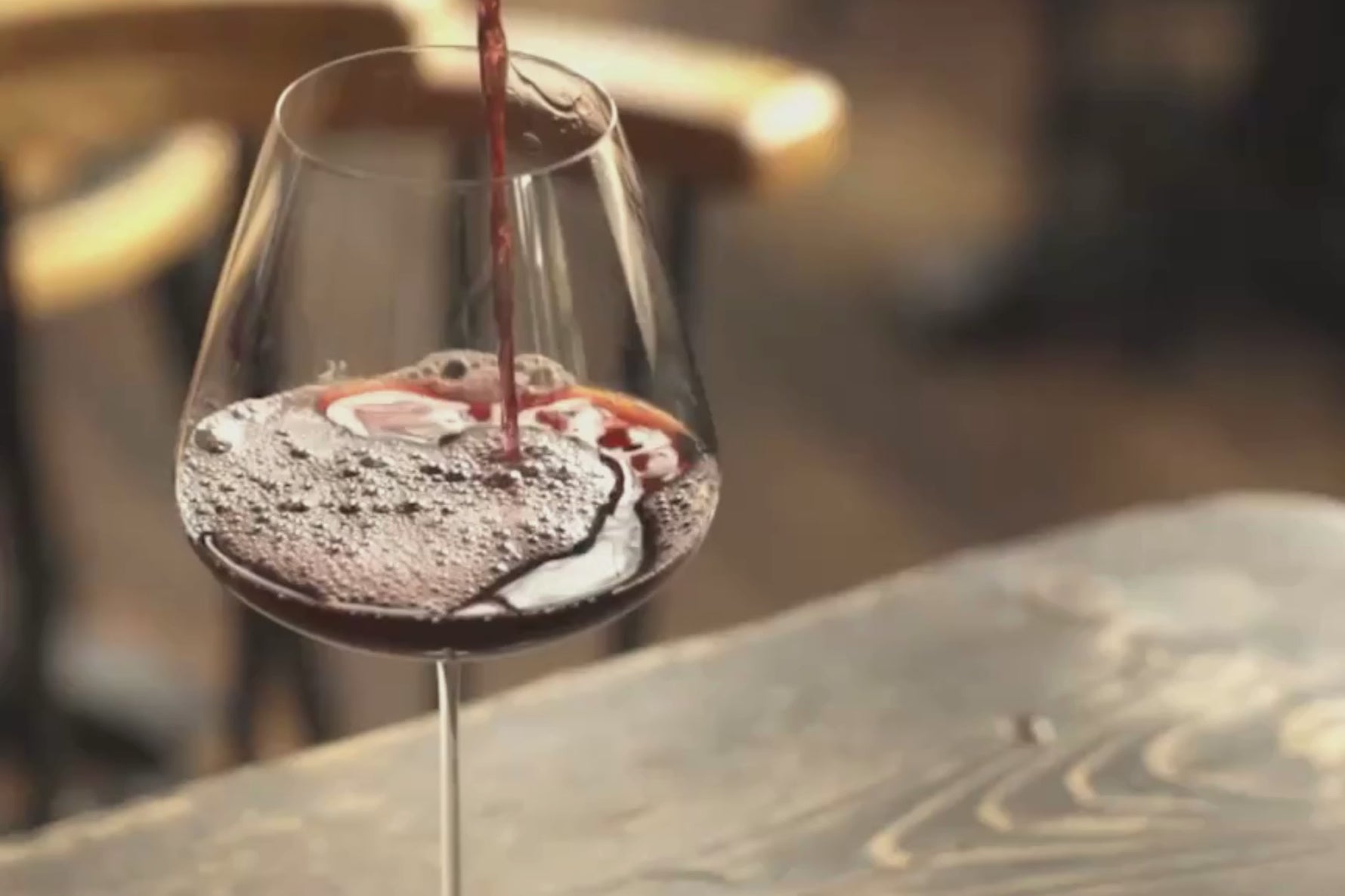 Honey Spencer pouring red wine into a NUDE Stem Zero glass at a sunlit restaurant table