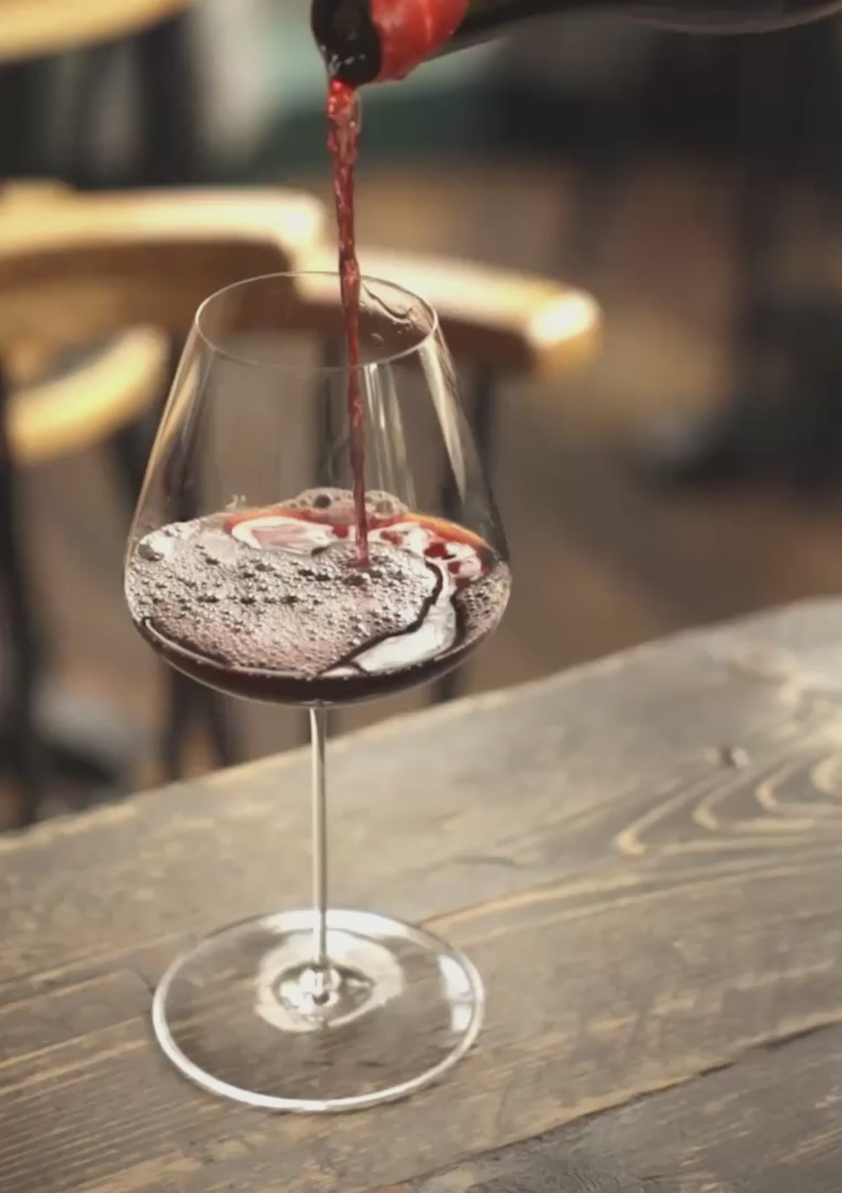 Honey Spencer pouring red wine into a NUDE Stem Zero glass at a sunlit restaurant table-mobile
